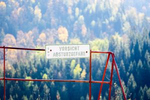 Blick auf Wald, davor ist ein Warnschild zu lesen mit dem Text „Vorsicht Absturzgefahr”