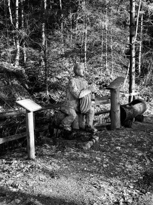 Blick aus der Ferne auf eine Holzskulptur eines Wanderers, der sich ausruht